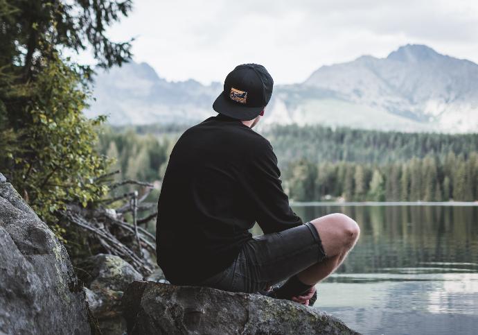 selective focus photography of man sitting on rock while looking at mountains